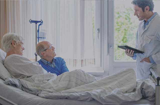 A man in hospital bed with wife, talking to doctor