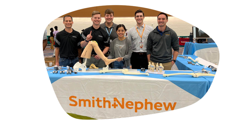 Blog-Engineering Day 2026-Paola tradeshow with knee in foreground.png